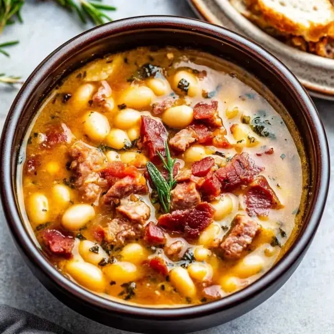 Un bol de soupe contenant des haricots blancs, des morceaux de viande et des herbes.