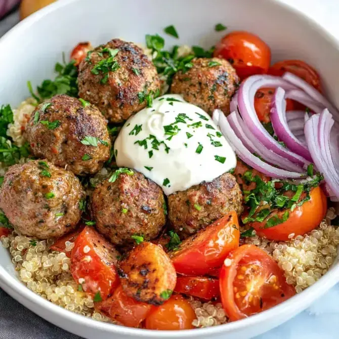 Un bol rempli de quinoa, de boulettes de viande, de tomates cerises, d'oignons rouges, garnies de yaourt nature et de persil frais.