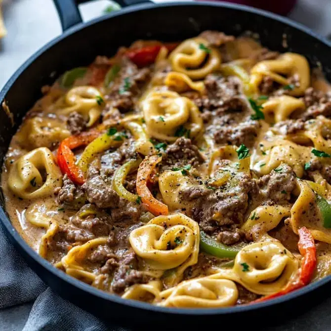 Un plat de tortellinis en sauce crémeuse mélangé avec de la viande hachée et des poivrons colorés dans une poêle.