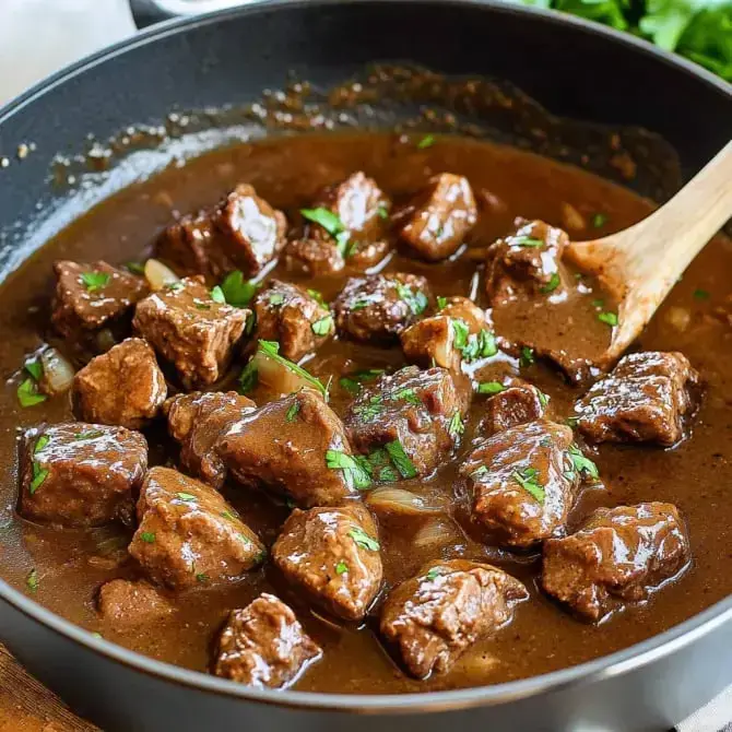 Un plat de viande en dés cuit dans une sauce brune, garni de persil, dans une casserole en bois.