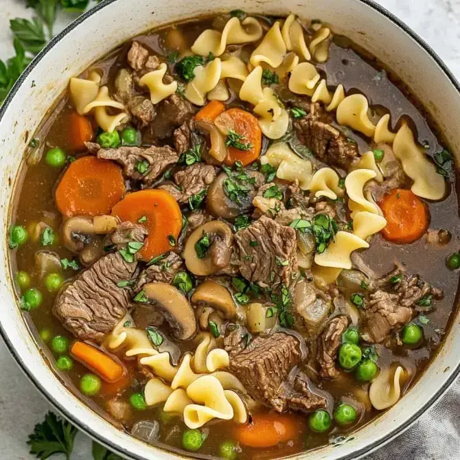 Un ragoût de viande avec des nouilles, des carottes, des petits pois et des champignons, servi dans une grande casserole.