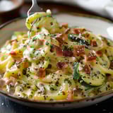 A bowl of pasta with bacon and zucchini.