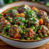 A bowl of meatballs with peas and tomatoes.