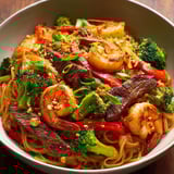 A bowl of noodles with shrimp, broccoli, and red peppers.
