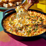 A person is holding a spoon with a piece of food on it.