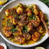 A bowl of chicken with a wooden spoon.