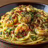 A bowl of spaghetti with shrimp and herbs.